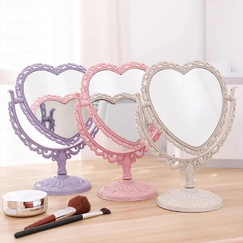 Un set de cuatro espejos de maquillaje con forma de corazón y doble cara en morado, rosa y blanco sobre una superficie de mad