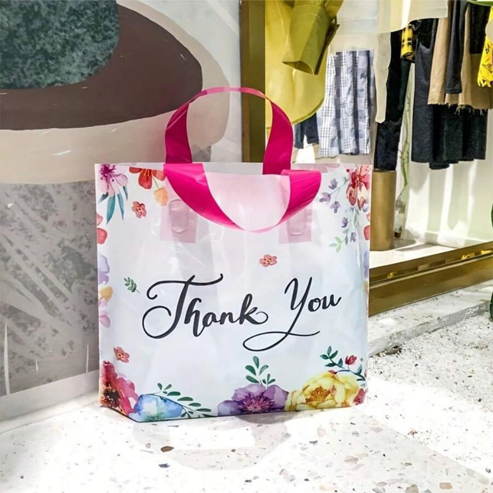 White floral thank you gift bags with pink handles displayed in a retail setting.