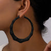 A close-up of black bamboo hoop earrings worn on a person's ear.