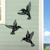 Black metal hummingbird wall decor set featuring three silhouettes on a light gray siding background