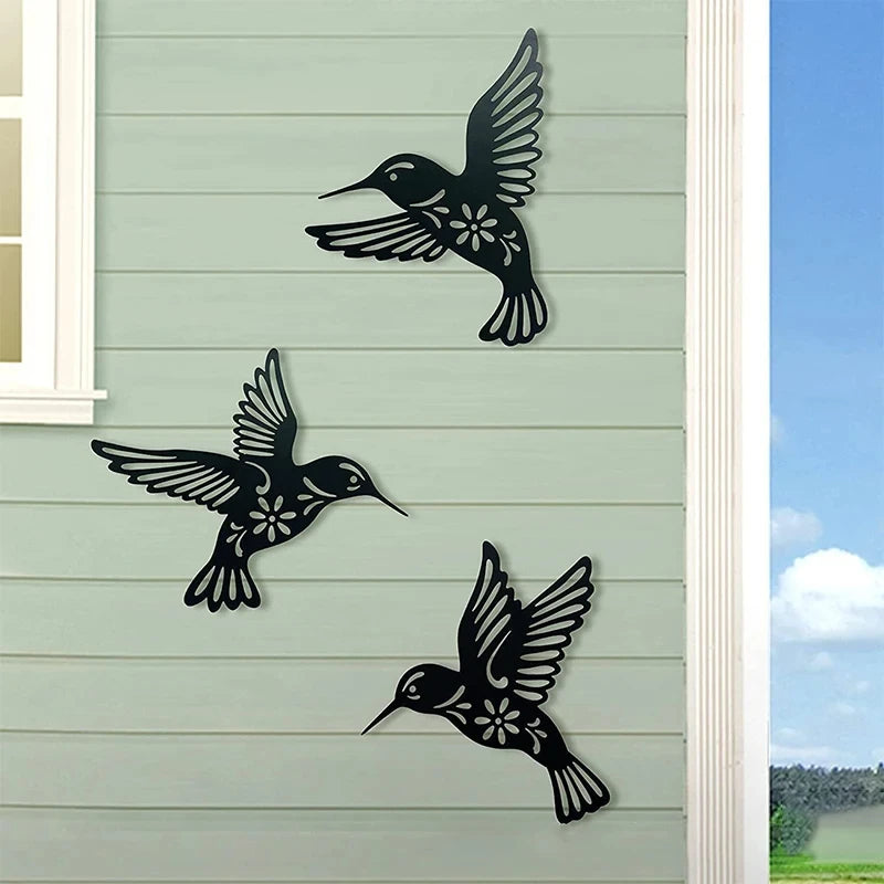 Black metal hummingbird wall decor set featuring three silhouettes on a light gray siding background