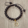 A handmade beaded bracelet featuring natural black stones and a gold charm with an infinity symbol.