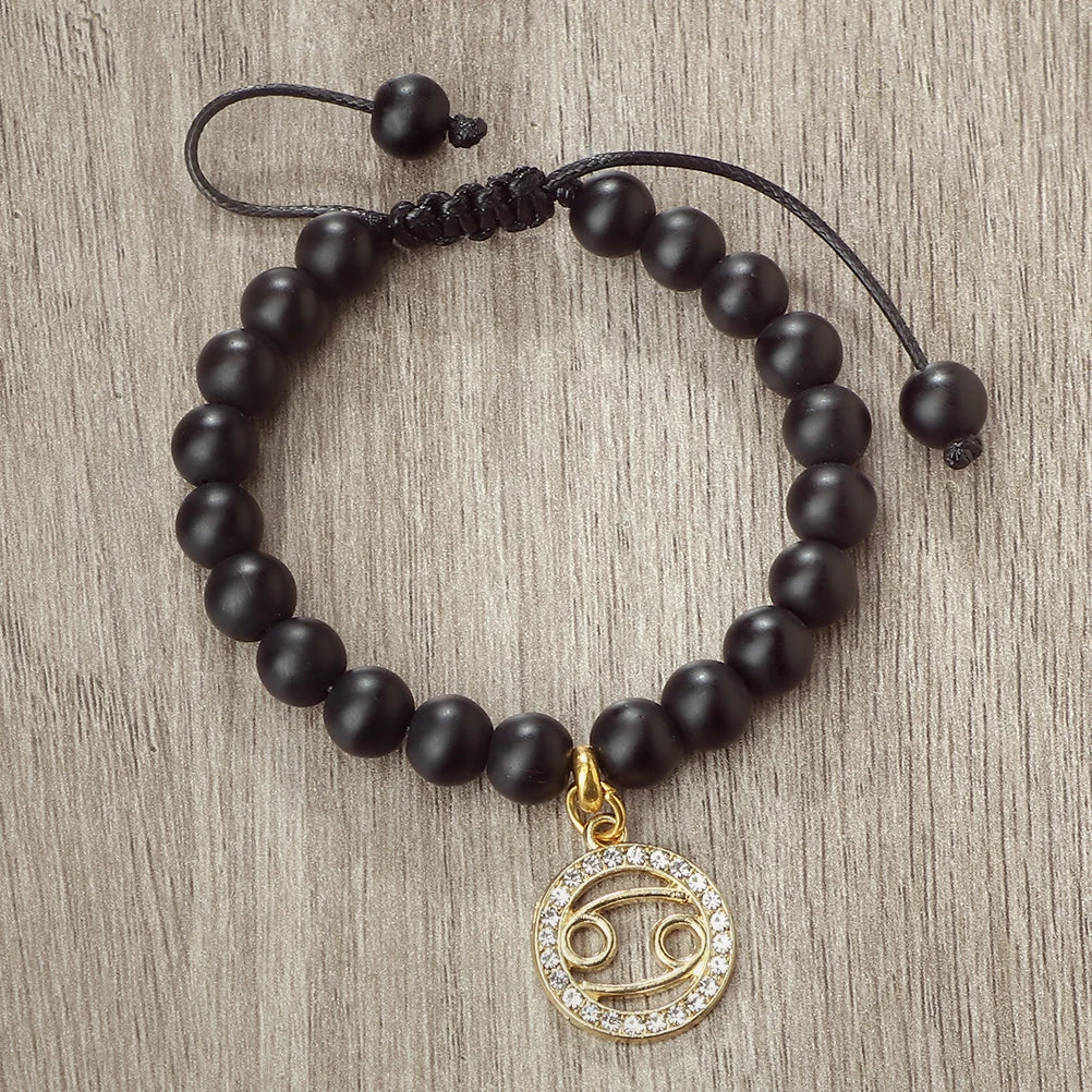 A handmade beaded bracelet featuring natural black stones and a gold charm with an infinity symbol.