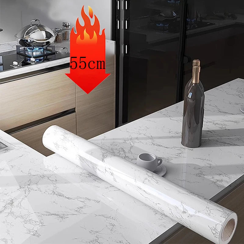 A roll of white marble self-adhesive wallpaper is displayed on a marble countertop next to kitchen cabinets.