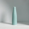 A tall, slender ceramic vase in a pale mint green color standing on a white surface.