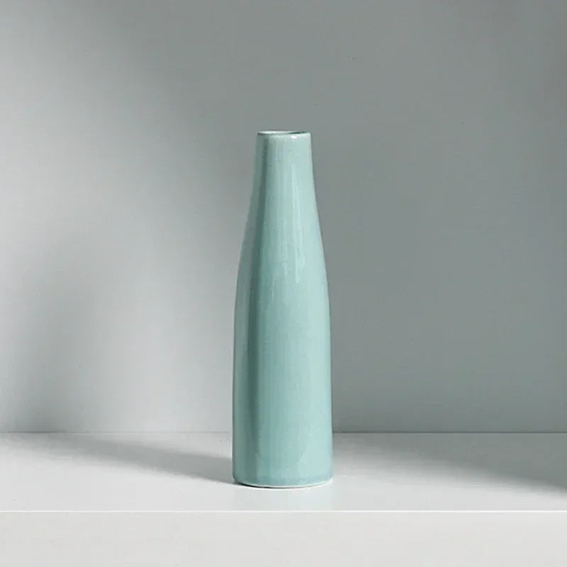 A tall, slender ceramic vase in a pale mint green color standing on a white surface.