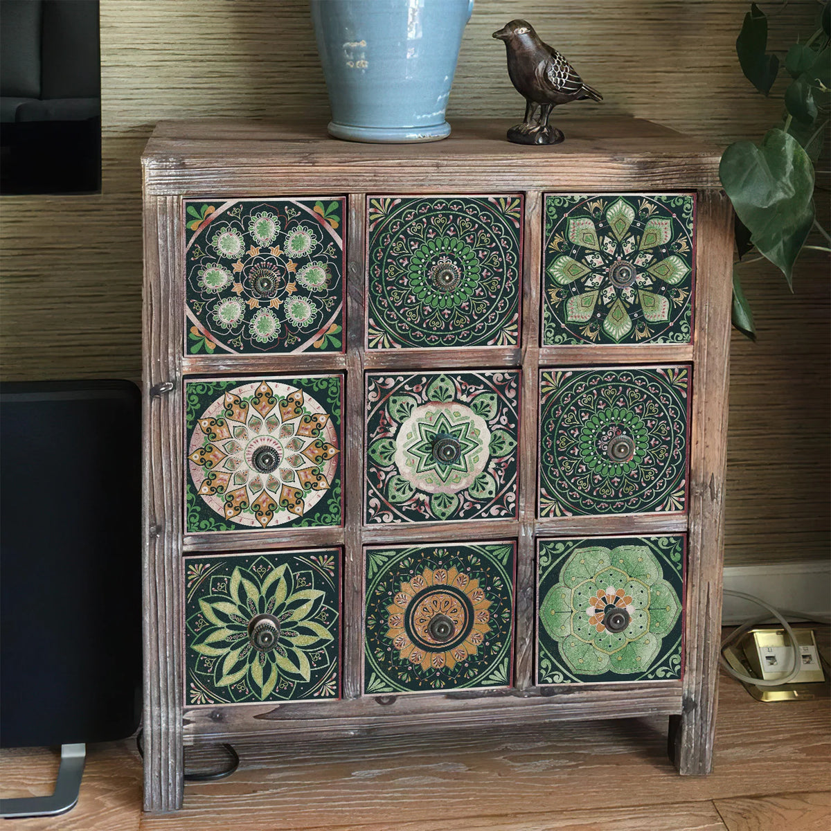 A wooden cabinet displaying various patterned self-adhesive tile wall stickers for kitchen and bath use.