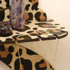 A gold chain necklace is displayed on a leopard print storage rack next to a purple crystal.