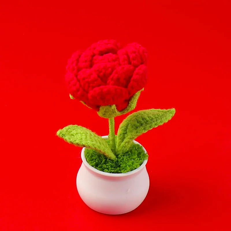 A hand woven crochet red peony flower potted in a pink ceramic cup against a red background.