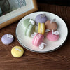 A collection of pastel-colored macaron-shaped soy wax candles arranged on a white plate.