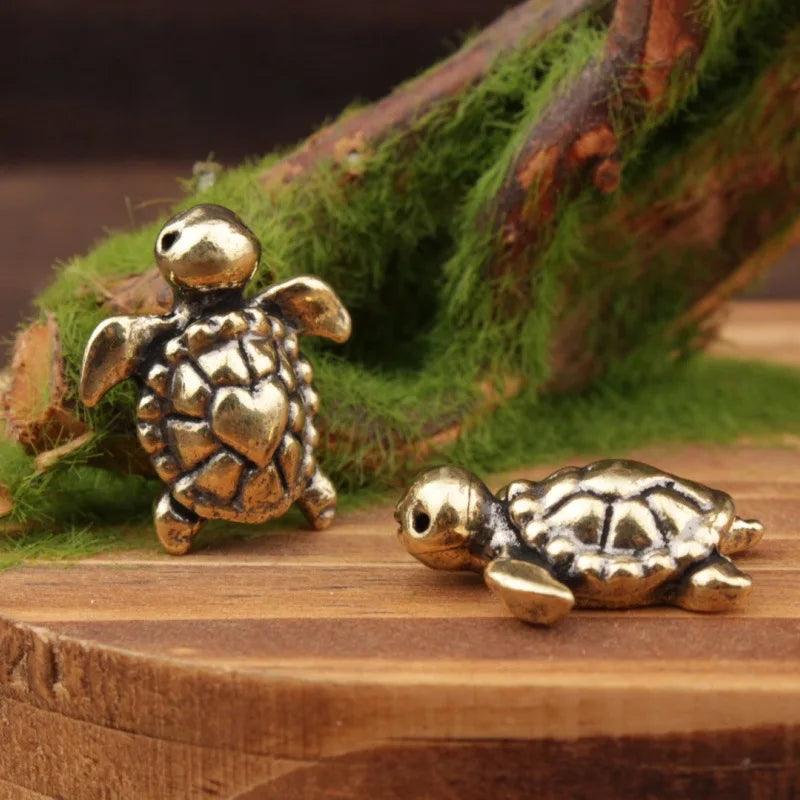 A handcrafted brass turtle figurine resting on a wooden surface next to mossy branches.