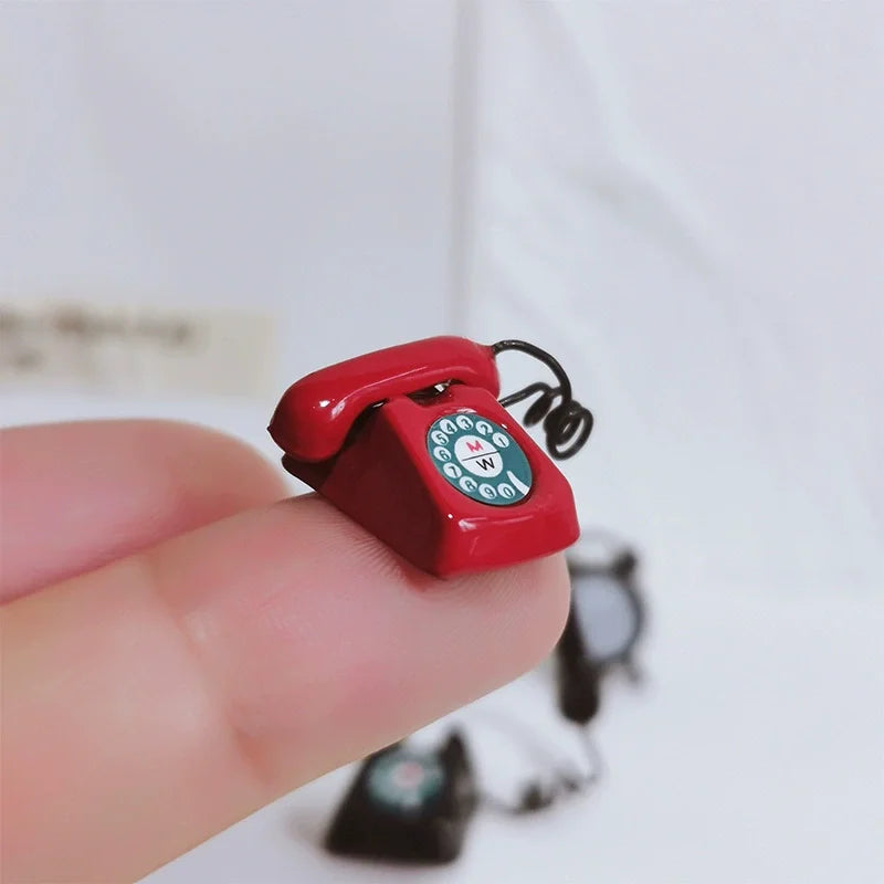 A red vintage rotary desk phone miniature decor is held between a person's fingers against a white background.