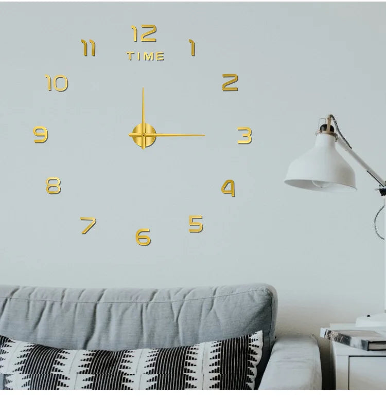 A modern wall clock with gold-colored numbers and hands is displayed on a light gray wall above a sofa.