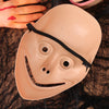 A light beige full face mask resembling a creepy evil clown, resting on a dark, textured surface.