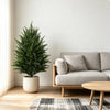 A potted artificial cedar topiary tree in a beige ceramic pot placed next to a light gray sofa and wooden table.