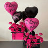 A display of heart-shaped balloons in pink and black, including a bouquet of pink roses wrapped in a pink gift box.