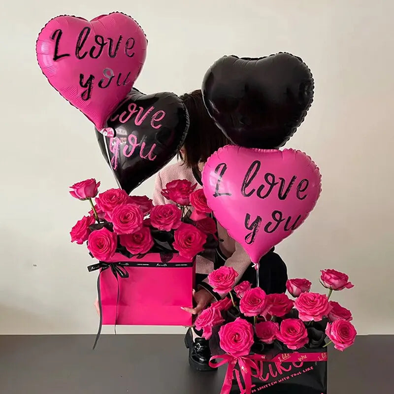 A display of heart-shaped balloons in pink and black, including a bouquet of pink roses wrapped in a pink gift box.