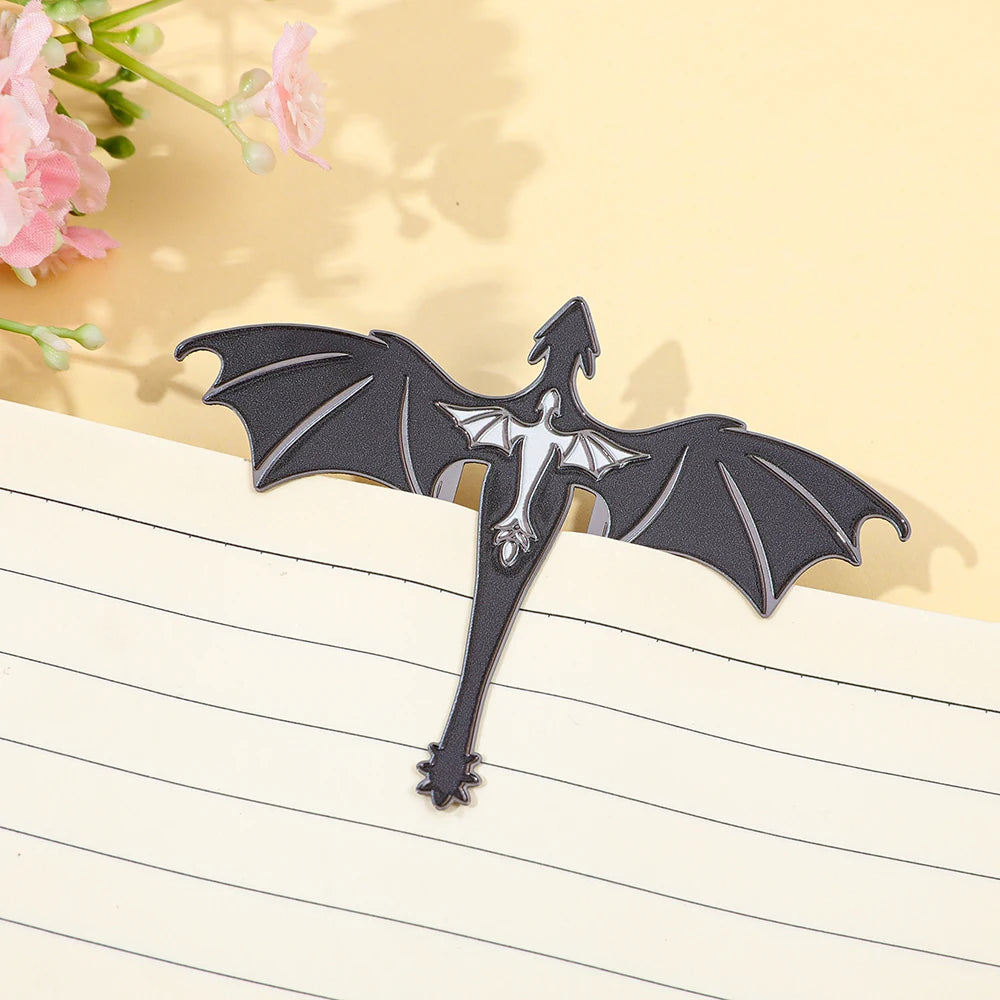 A black metal bookmark shaped like a four-winged dragon with a silhouette of a bat inside