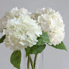 A bouquet of large white artificial hydrangea flowers with green leaves.