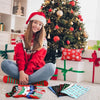 A woman sits in front of a decorated Christmas tree surrounded by wrapped gifts and colorful socks.