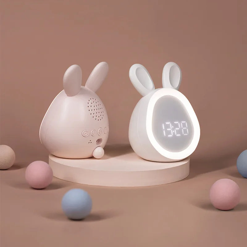 A pink mini LED cartoon alarm clock night light with rabbit ears sitting on a round stand.