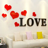 Red acrylic heart wall stickers with mirror finish displayed on a white wall above a sofa.