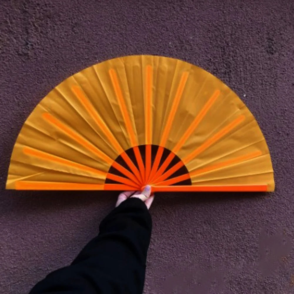 A hand is opening a yellow Tai Chi performance fan with orange ribs against a purple wall.