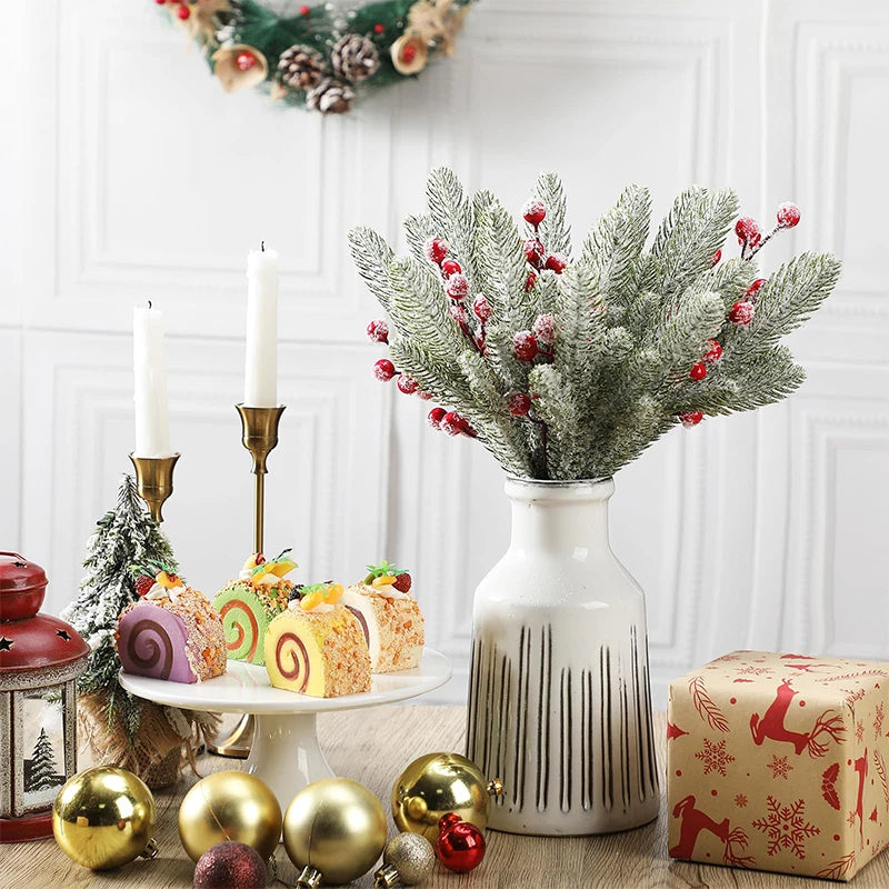 A white ceramic vase holds a bouquet of frosted pine needles and red berries on a wooden surface.