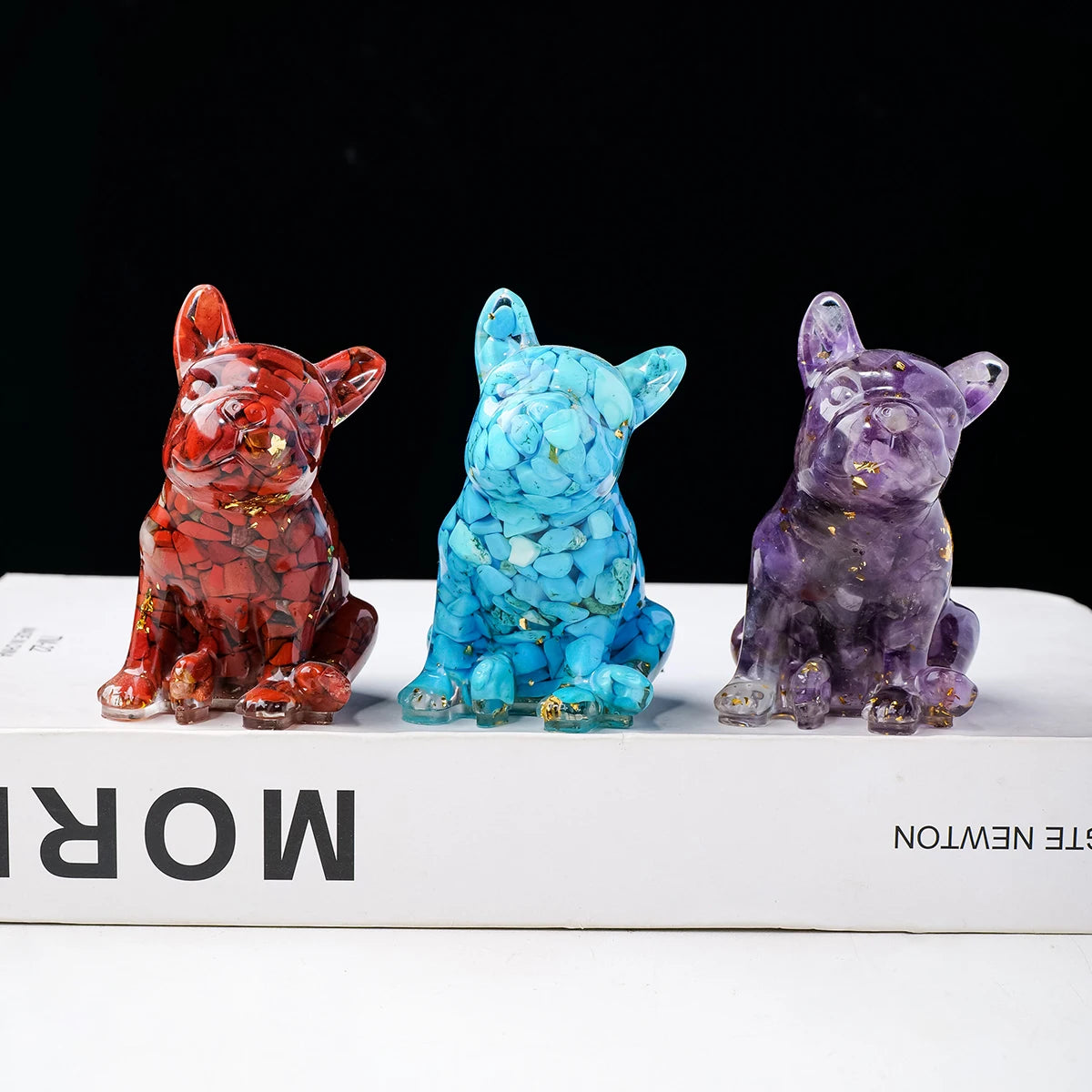 Three crystal dog statues in red, blue, and purple sitting on a white book.