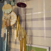 A collection of hanging wind chimes featuring wooden and metal bells in gold and silver tones against a light plaid backgroun