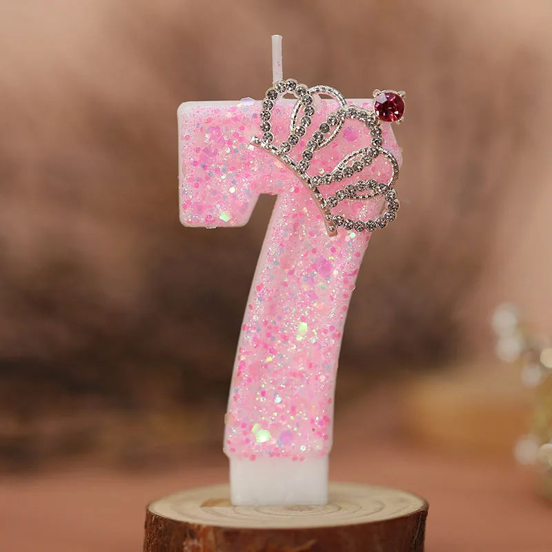 A pink glitter number seven candle with a silver crown topper on a wooden base.