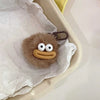 A cute plush sausage-mouth keychain with large white eyes and a tan mouth is placed in crumpled white tissue paper.