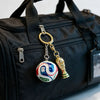 A gold and white FIFA trophy keychain attached to a black fabric bag.