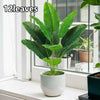 A vibrant green artificial Bird of Paradise plant in a white pot sitting on a windowsill.