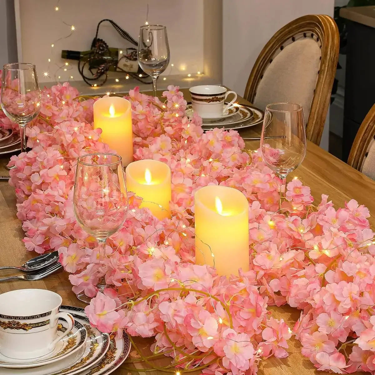 A table setting decorated with a pink cherry blossom string lights garland and glassware.