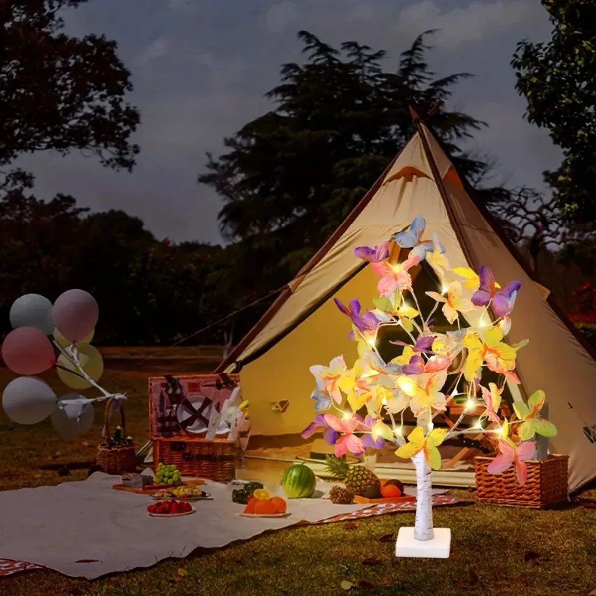 A large canvas tent illuminated by a tree-shaped light fixture featuring colorful butterfly lights in an outdoor setting.