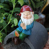 Keramische dekorative Gnome-Statue mit rotem Hut, weißem Bart und blauem Gewand auf grauem Stein.