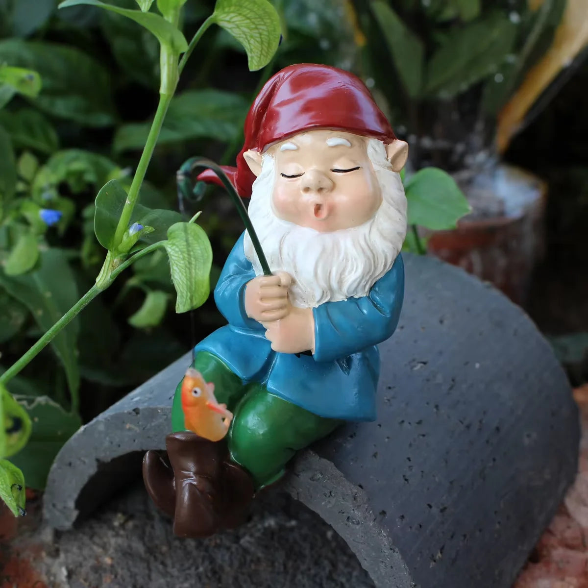 Keramische dekorative Gnome-Statue mit rotem Hut, weißem Bart und blauem Gewand auf grauem Stein.