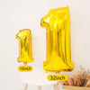A large gold foil number balloon shaped like the number one standing next to a smaller gold foil number one on a white table.