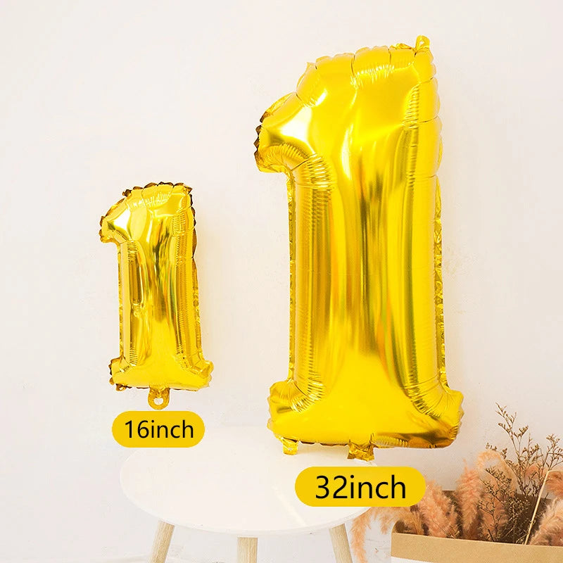 A large gold foil number balloon shaped like the number one standing next to a smaller gold foil number one on a white table.