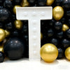 A white marquee light-up letter T is displayed against a background of black and gold balloons.