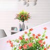 A vibrant bouquet of artificial flowers in various shades of red, pink, and yellow displayed against a white wooden backgroun