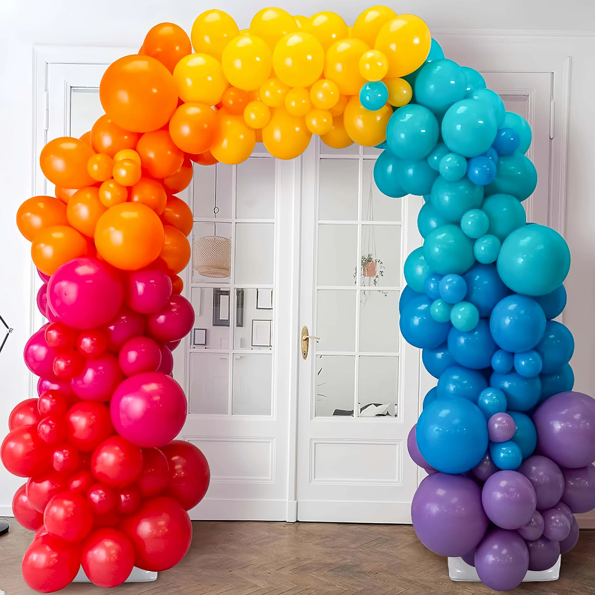 A decorative balloon arch kit featuring bright orange, yellow, and blue balloons framing a white door.