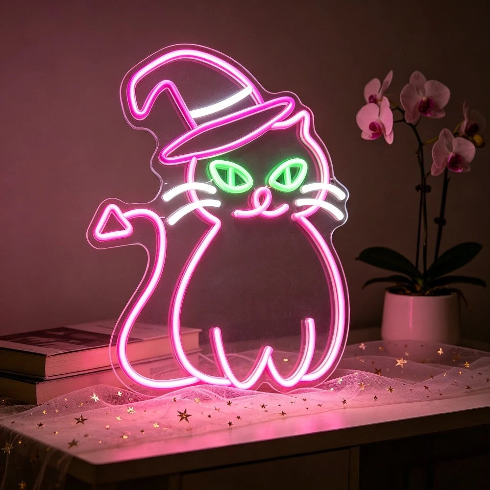 A glowing neon light sign shaped like a cat wearing a witch hat, illuminating a pink surface.