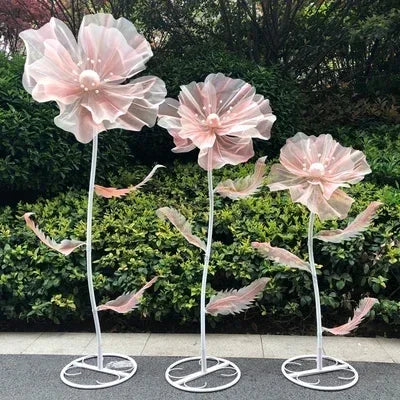A set of three large pink velvet mesh flowers on white stems used for wedding decoration.