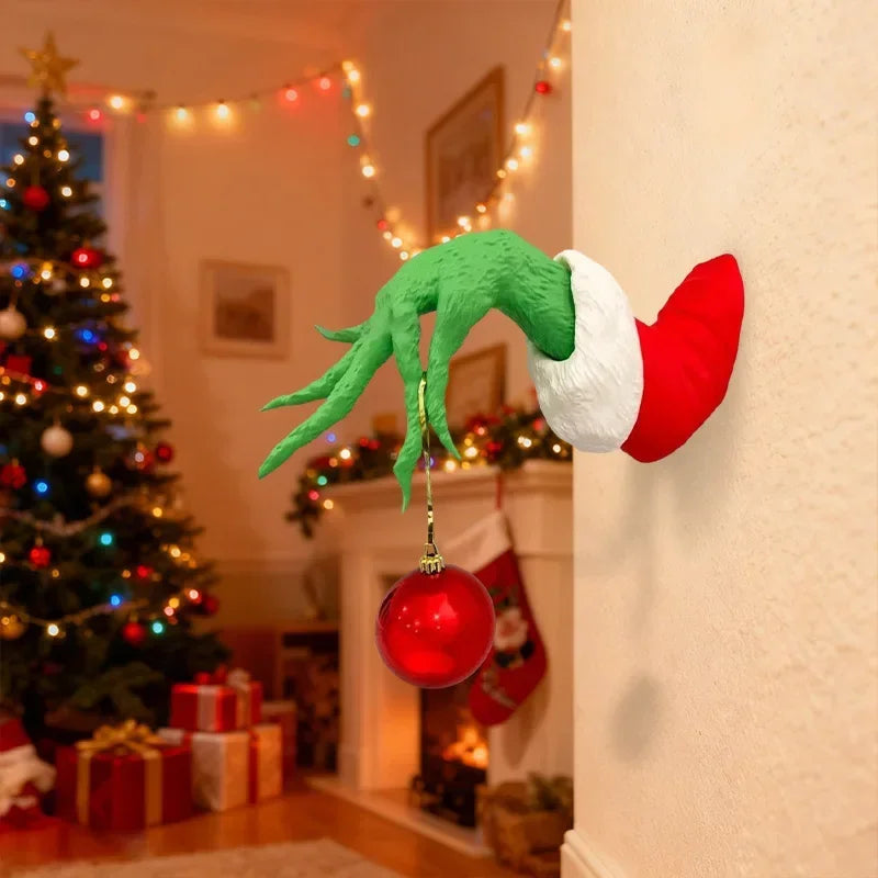 Green monster arm wall decor with a red and white Santa hat hanging on a cream-colored wall.