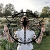 A person holds up an elegant black dragonfly metal wall art piece outdoors.
