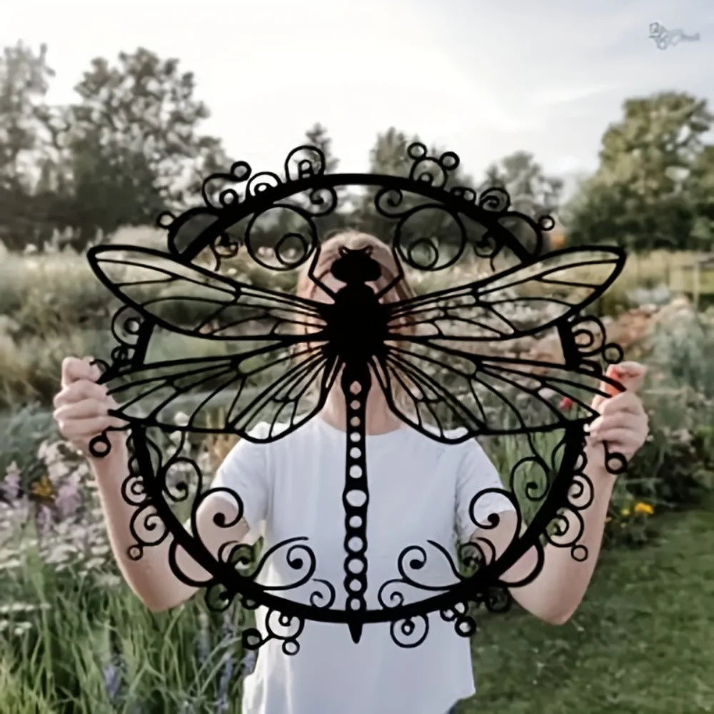 A person holds up an elegant black dragonfly metal wall art piece outdoors.