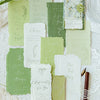 A collection of vintage old English manuscript decor paper in sage green and cream tones arranged on white lace.