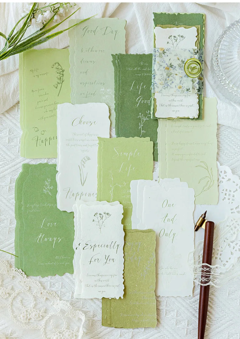 A collection of vintage old English manuscript decor paper in sage green and cream tones arranged on white lace.